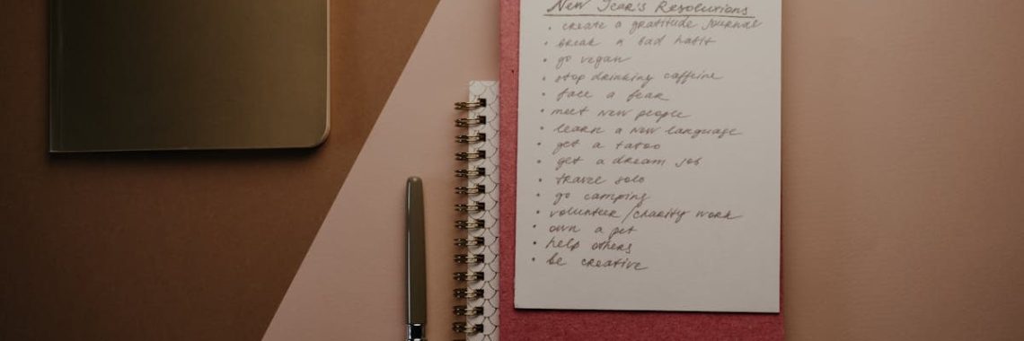 Top view of a cozy pink notebook with New Year resolutions, pen, and stylish paperclip setup.